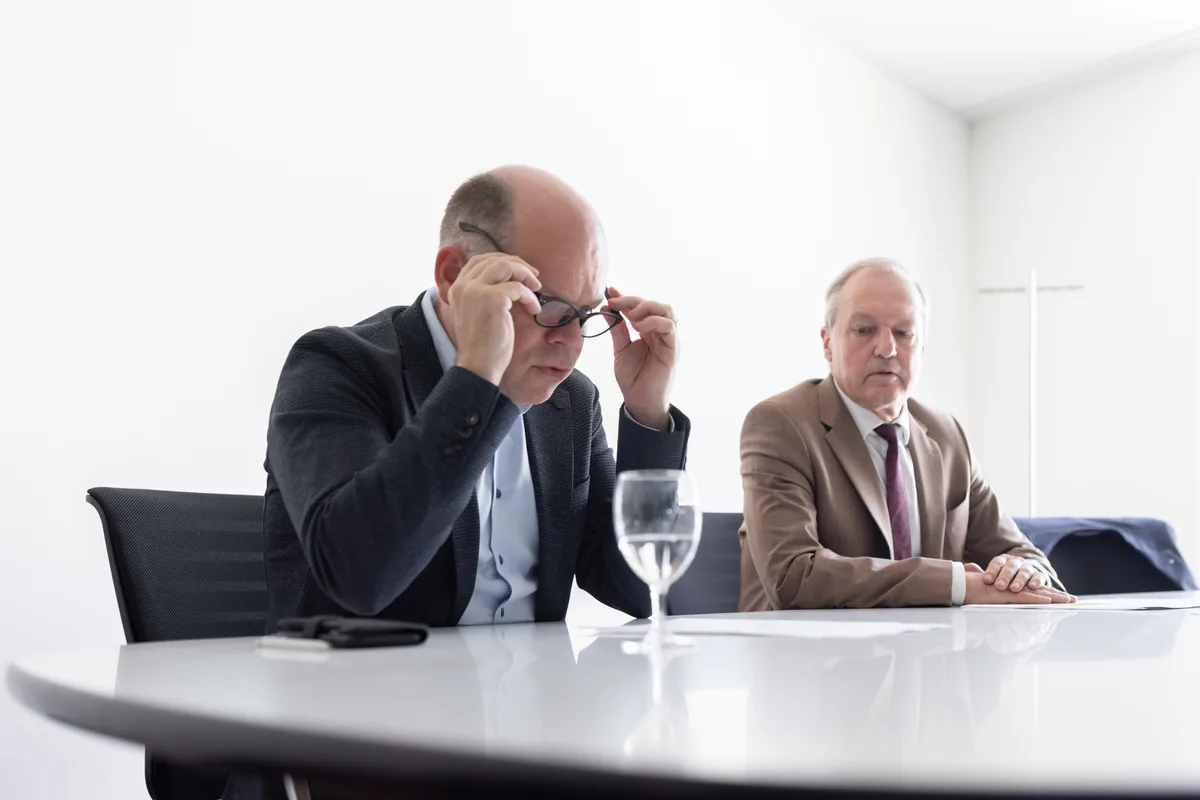 Zwei Männer sitzen an einem Sitzungstisch.